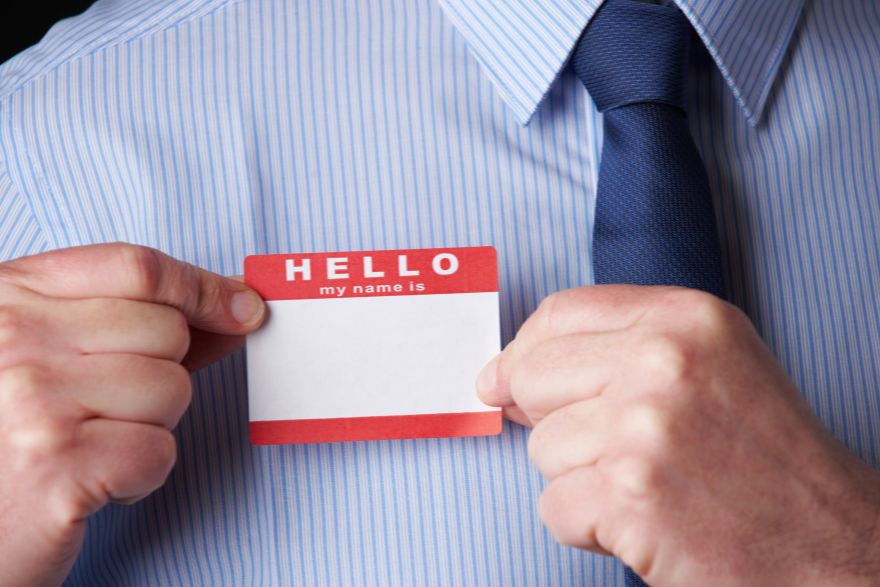 red name tag on a man wearing light blue formal shirt and blue tie.