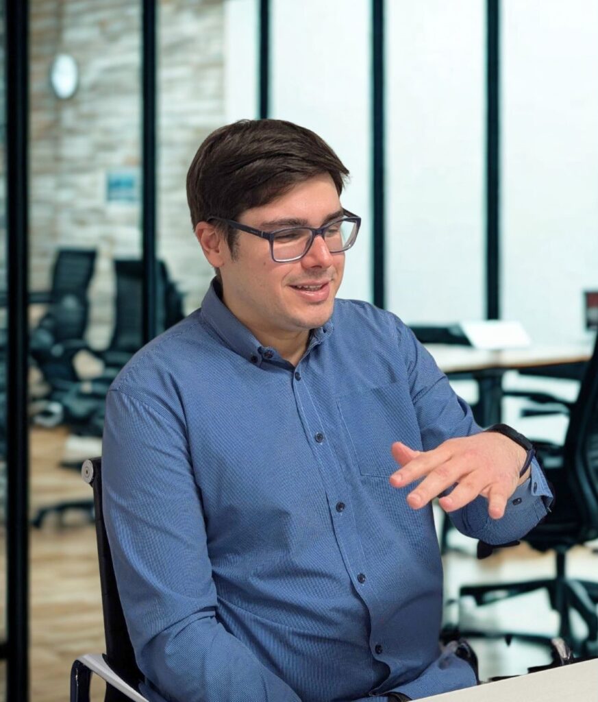 A man, potentially a MEXT scholar from Brazil, in an office setting, gesturing while speaking. The image relates to Daijob.com's "Real Success Stories," focusing on "Transitioning to a Career in Japan: Lessons from a MEXT Scholar." It aligns with an expat career guide, covering topics like interviews, language proficiency (BJT 2, JLPT 2), and the experience of working in Japan, particularly for Japanese or Business Japanese speakers, possibly reflecting his journey as a recruitment consultant.
