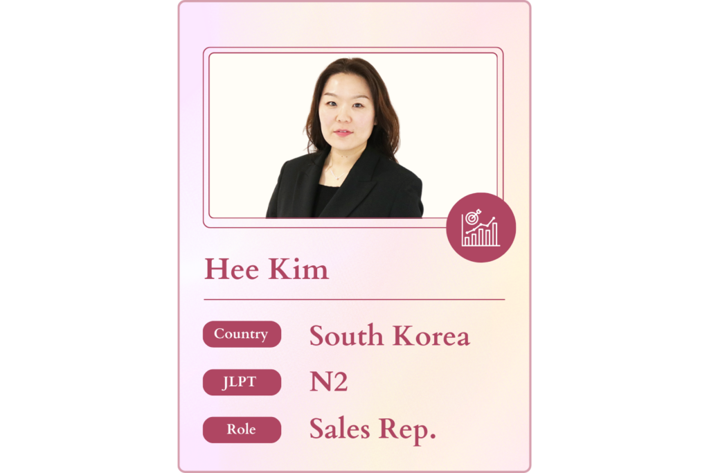 A stylized graphic resembling a trading card featuring Hee Kim, a Sales Rep from South Korea with JLPT N2 certification. The card design incorporates a pink and white color scheme with an icon of a target and upward-trending graphs. Relevant for an expat career guide, offering advice on overseas opportunities, dream jobs in Japan, and networking meetups for foreigners through Daijob.